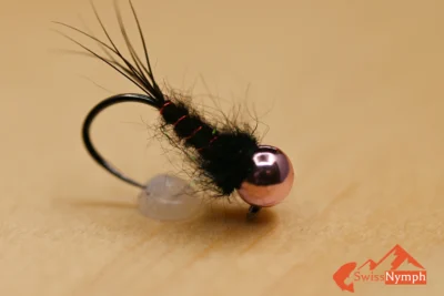 Eine extrem fängige Wettkampf-Nymphe nach M. Šenkýř (Europameister und Vizeweltmeister der Masters-Gruppe) mit rosa Tungstenkopf, Nerz-Dubbingkörper und roter Rippung. Sie sinkt schnell, arbeitet lebendig in der Drift und triggert zuverlässig Bisse auf Forellen, Äschen und auch Weissfische – in Fluss wie See.