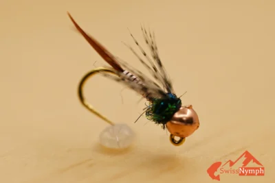 Die Copper John Nymphe ist ein moderner Klassiker im Fliegenfischen und hat sich als universelles Muster für Forellen und Äschen in unterschiedlichsten Gewässern bewährt. Dank ihres kupfernen Drahtkörpers sinkt sie besonders schnell – ideal für tiefe Gumpen, starke Strömung oder als Ankerfliege beim Czech Nymphing.