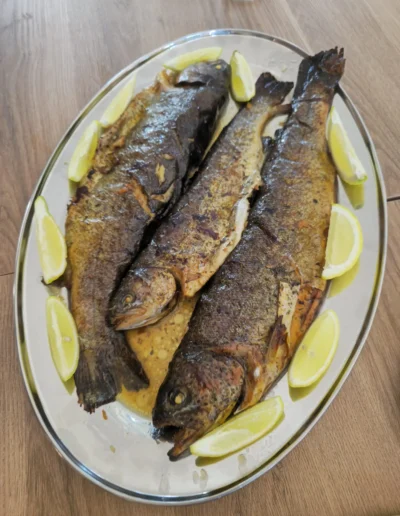 Plate of grilled whole fish with crispy skin, lemon wedges around on a wooden table.